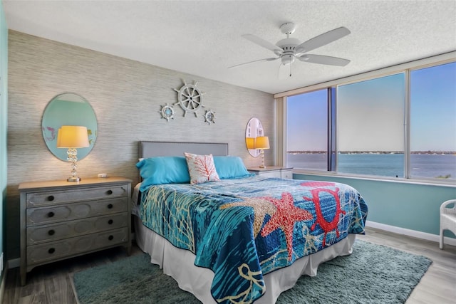 bedroom with baseboards, wood finished floors, a water view, a textured ceiling, and multiple windows