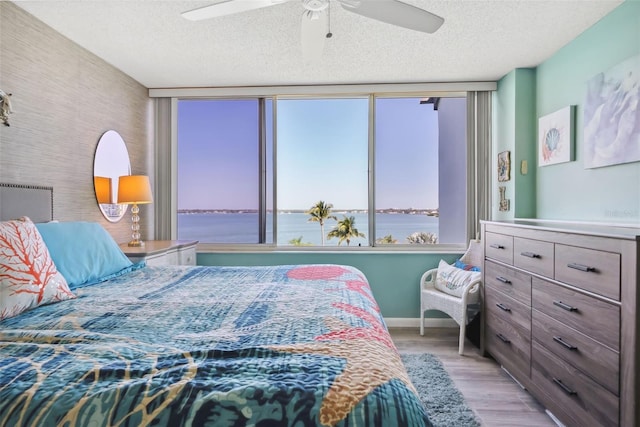 bedroom with a water view, light wood-type flooring, a ceiling fan, and a textured ceiling