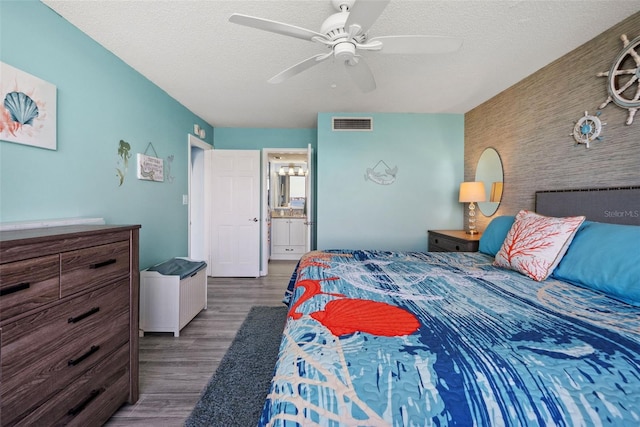 bedroom with a textured ceiling, an accent wall, wood finished floors, and visible vents