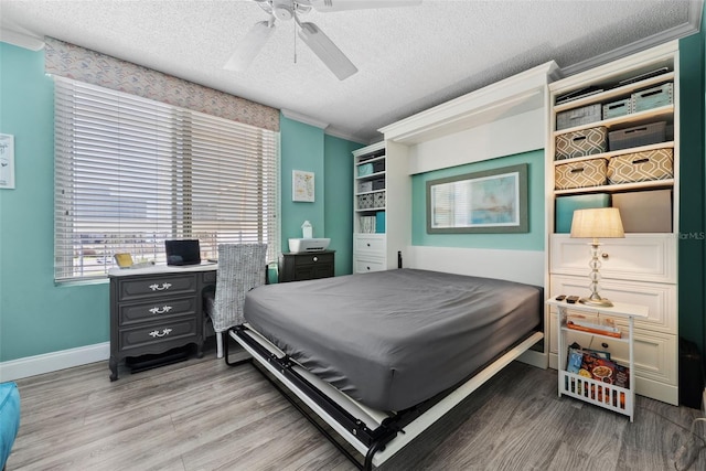 bedroom featuring light wood finished floors, baseboards, a ceiling fan, ornamental molding, and a textured ceiling