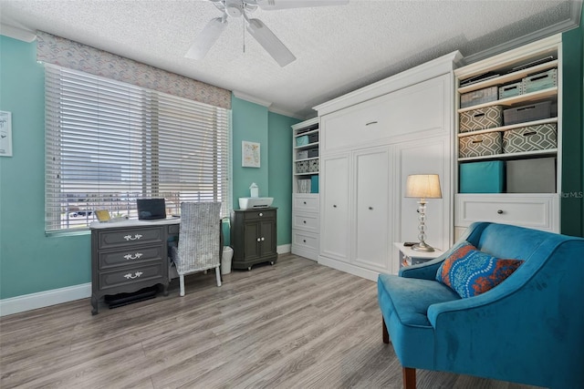 sitting room with light wood finished floors, baseboards, ceiling fan, a textured ceiling, and crown molding