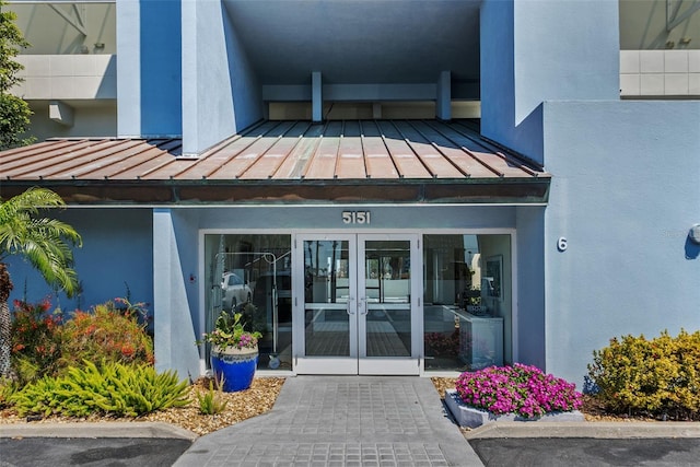 view of exterior entry featuring a standing seam roof, metal roof, stucco siding, and french doors