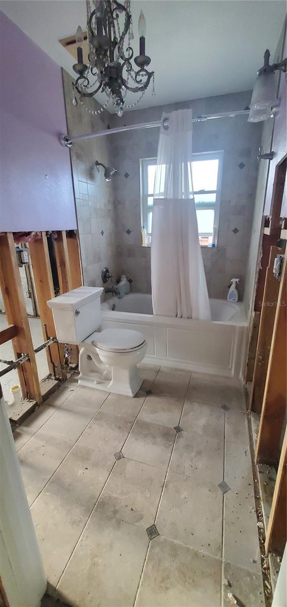 bathroom featuring shower / bathtub combination with curtain, toilet, and an inviting chandelier