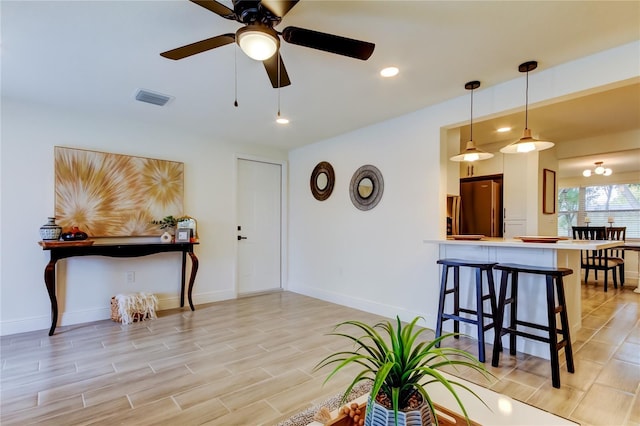 interior space with decorative light fixtures, stainless steel fridge, a kitchen bar, ceiling fan, and kitchen peninsula