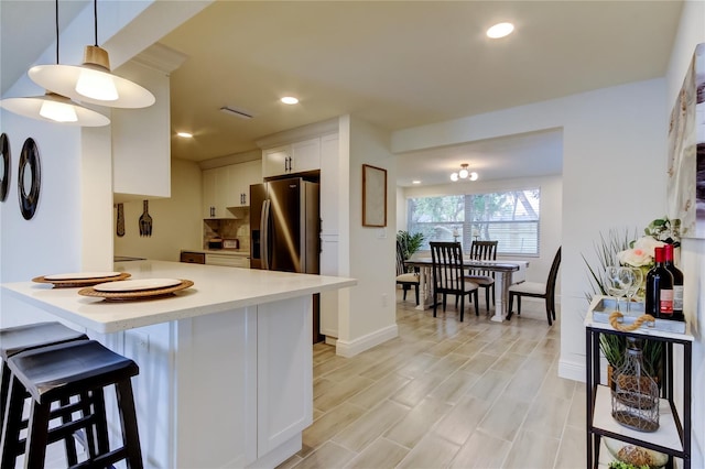 kitchen featuring white cabinets, a kitchen bar, stainless steel fridge with ice dispenser, decorative light fixtures, and kitchen peninsula