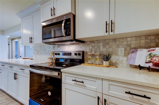 kitchen with stainless steel appliances, light stone countertops, light hardwood / wood-style floors, white cabinets, and decorative backsplash