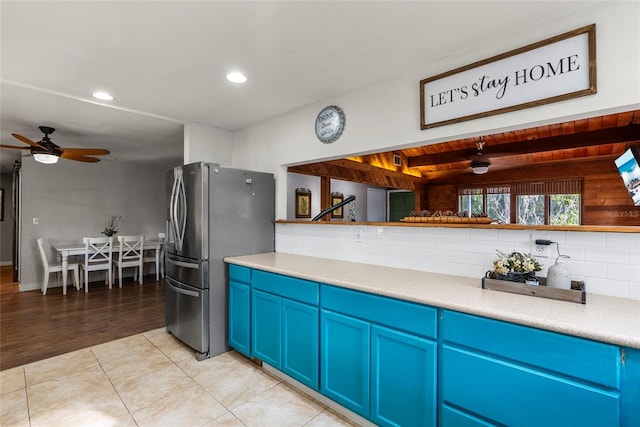 kitchen with stainless steel refrigerator, light tile patterned floors, blue cabinetry, and backsplash