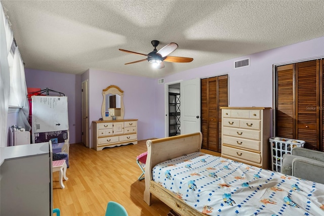 bedroom featuring ceiling fan, two closets, a textured ceiling, and light wood-type flooring