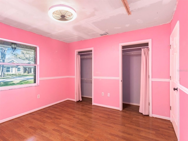 unfurnished bedroom featuring hardwood / wood-style flooring and two closets