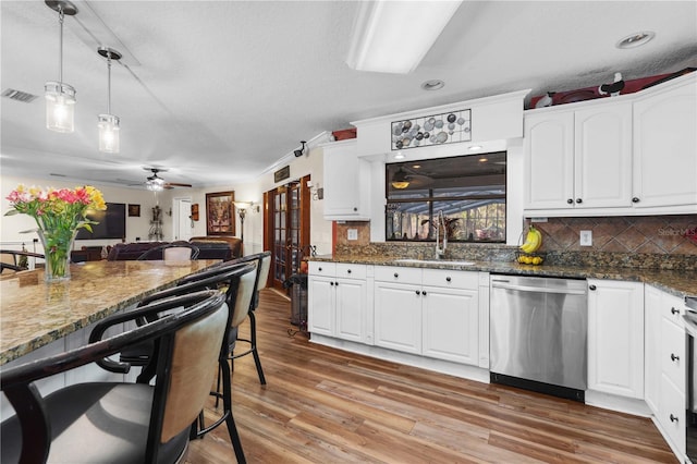 kitchen with dishwasher, sink, white cabinets, dark stone counters, and hanging light fixtures