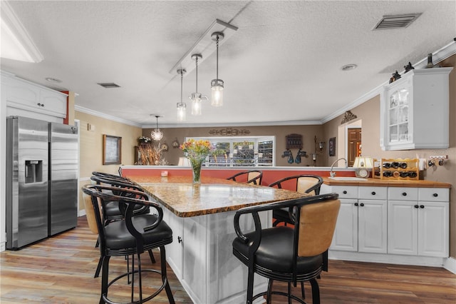 kitchen with white cabinetry, stainless steel fridge, a kitchen bar, and decorative light fixtures