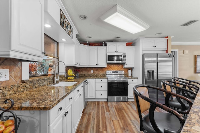 kitchen featuring white cabinetry, sink, dark stone counters, stainless steel appliances, and crown molding