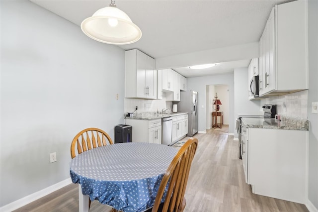 kitchen featuring appliances with stainless steel finishes, light stone countertops, light hardwood / wood-style flooring, and white cabinets