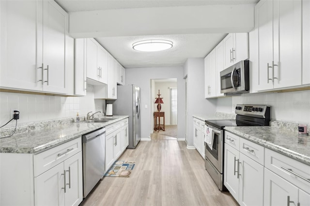 kitchen featuring appliances with stainless steel finishes, white cabinets, decorative backsplash, light stone countertops, and light wood-type flooring