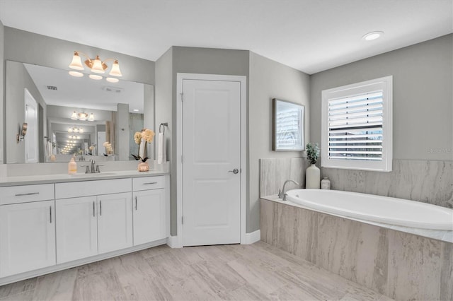 bathroom featuring a relaxing tiled tub, vanity, and a notable chandelier