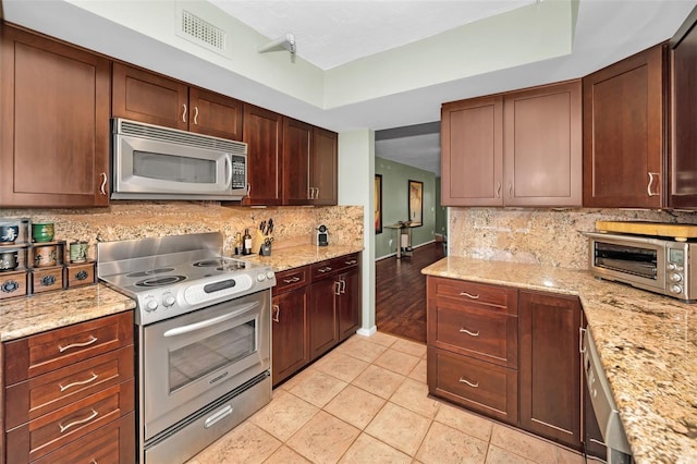 kitchen with stainless steel appliances, light tile patterned floors, light stone counters, and decorative backsplash