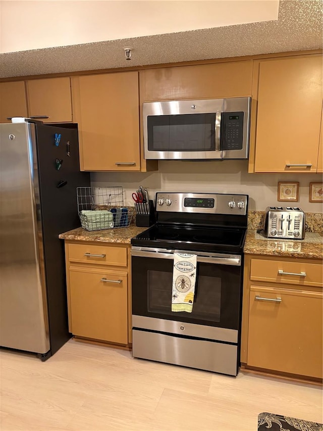 kitchen with stainless steel appliances, stone counters, a textured ceiling, and light hardwood / wood-style flooring