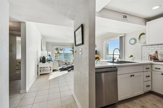 kitchen with light tile patterned flooring, sink, white cabinetry, stainless steel dishwasher, and decorative backsplash