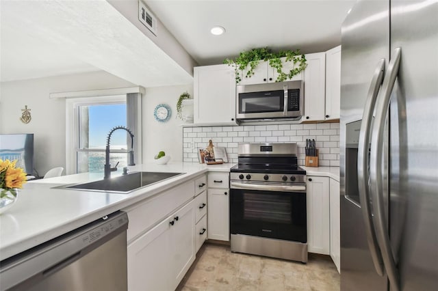 kitchen featuring sink, white cabinetry, stainless steel appliances, decorative backsplash, and kitchen peninsula