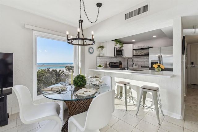 tiled dining space featuring a water view, sink, and a notable chandelier