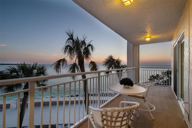 balcony at dusk featuring a water view