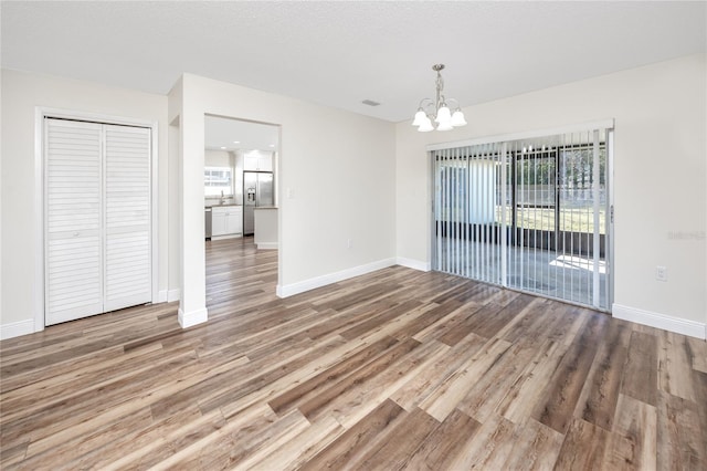 unfurnished dining area with wood-type flooring and a notable chandelier