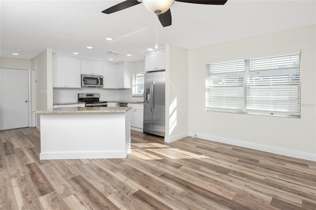 kitchen with a kitchen island, appliances with stainless steel finishes, a wealth of natural light, white cabinets, and light stone countertops