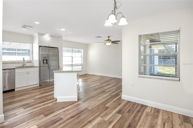 kitchen with decorative light fixtures, stainless steel appliances, a center island, and white cabinets