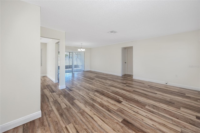 empty room with a notable chandelier, hardwood / wood-style flooring, and a textured ceiling