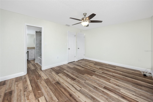 unfurnished bedroom featuring hardwood / wood-style floors, connected bathroom, a textured ceiling, and ceiling fan