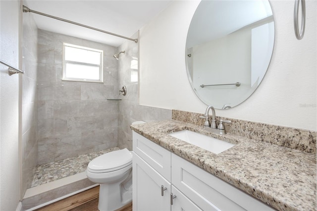 bathroom featuring vanity, toilet, hardwood / wood-style floors, and a tile shower