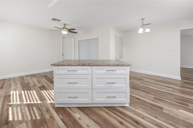 kitchen featuring light stone countertops, light wood-type flooring, a kitchen island, and white cabinets