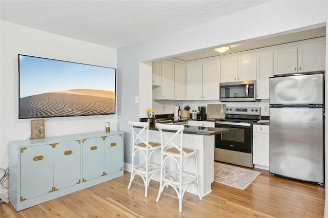 kitchen with appliances with stainless steel finishes, kitchen peninsula, light wood-type flooring, and white cabinets