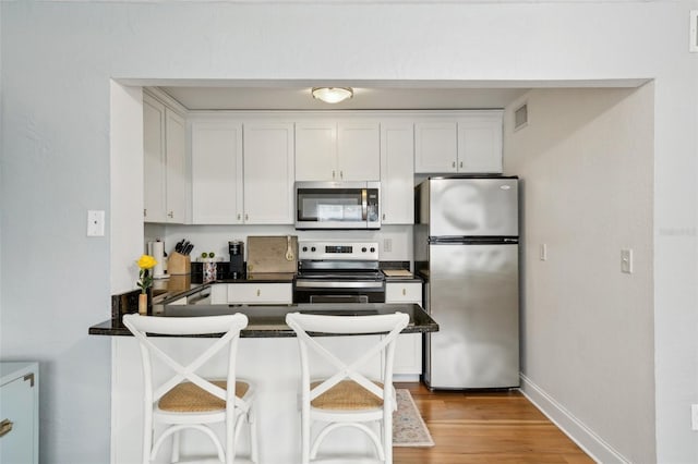 kitchen featuring a kitchen bar, light wood-type flooring, appliances with stainless steel finishes, kitchen peninsula, and white cabinets