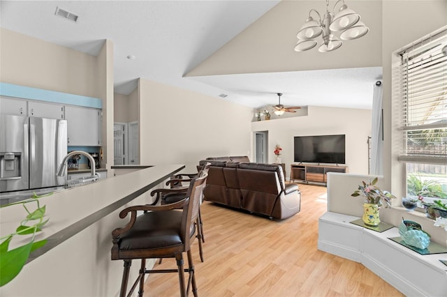 living room featuring ceiling fan with notable chandelier, sink, light hardwood / wood-style floors, and vaulted ceiling