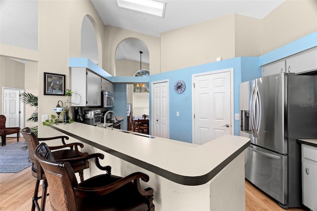 kitchen with sink, appliances with stainless steel finishes, high vaulted ceiling, light hardwood / wood-style floors, and kitchen peninsula