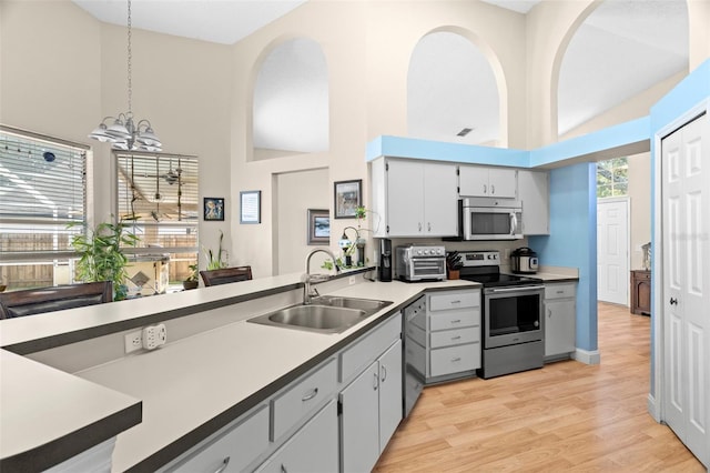 kitchen featuring sink, appliances with stainless steel finishes, hanging light fixtures, high vaulted ceiling, and light hardwood / wood-style floors