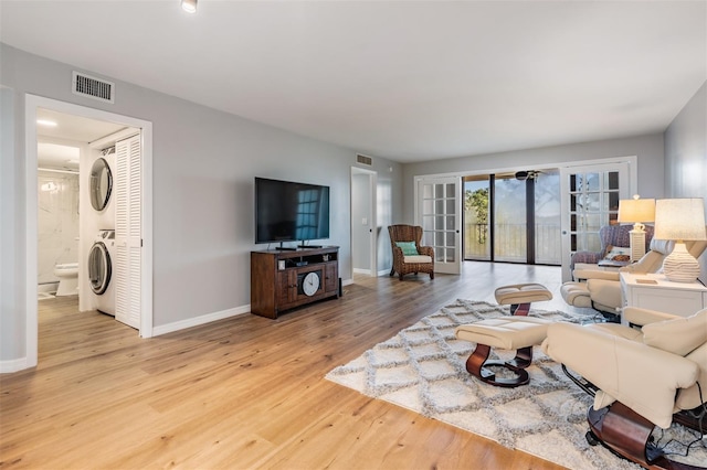 living room featuring visible vents, baseboards, french doors, stacked washing maching and dryer, and light wood finished floors