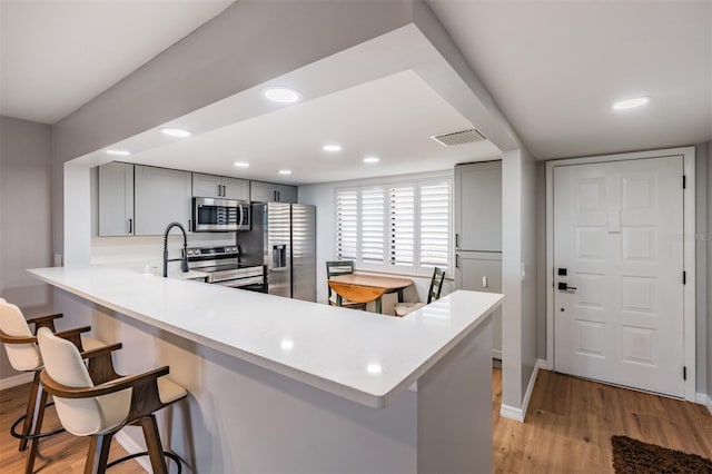 kitchen featuring a breakfast bar, stainless steel appliances, light countertops, gray cabinetry, and light wood-style floors