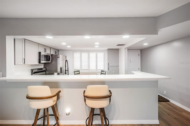 kitchen featuring visible vents, light countertops, appliances with stainless steel finishes, dark wood-style floors, and a kitchen bar