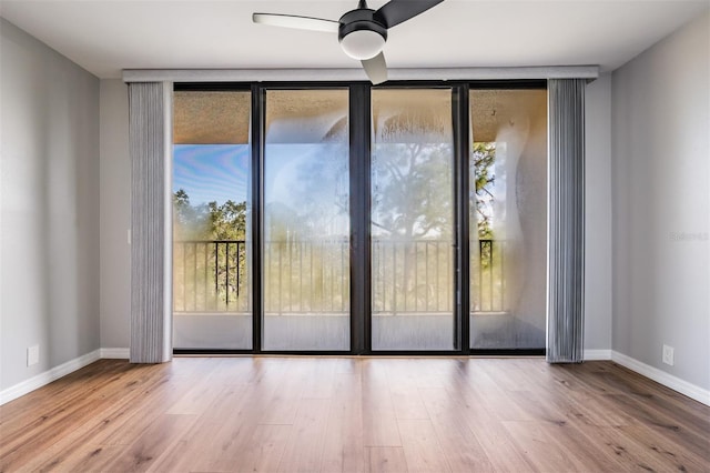 interior space with expansive windows, ceiling fan, baseboards, and wood finished floors