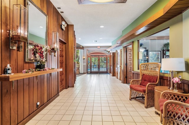 corridor featuring wood walls, a textured ceiling, and light tile patterned flooring