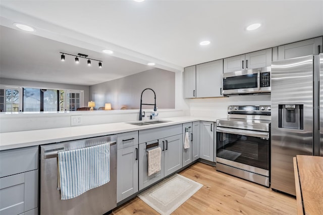 kitchen featuring stainless steel appliances, a sink, light wood-style flooring, and gray cabinetry