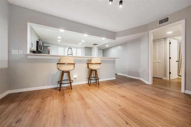 kitchen with visible vents, stainless steel microwave, light wood-style floors, a peninsula, and a kitchen bar