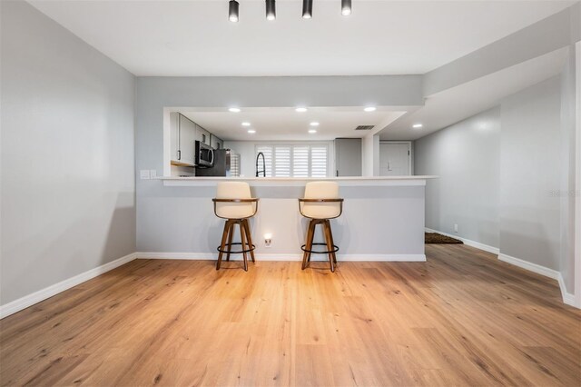 kitchen featuring baseboards, stainless steel microwave, a peninsula, light wood-type flooring, and a kitchen bar