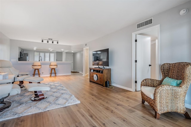 living area with light wood-type flooring, rail lighting, visible vents, and baseboards