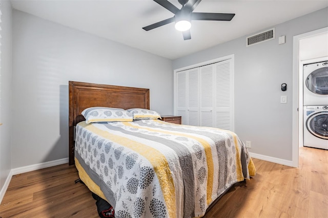 bedroom with wood finished floors, visible vents, baseboards, stacked washer / drying machine, and a closet