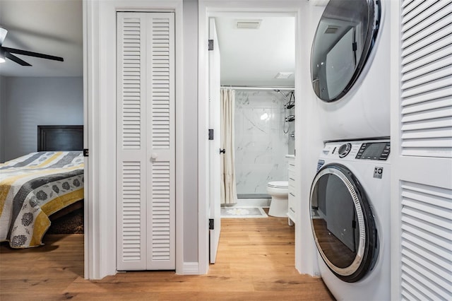 washroom with stacked washer and dryer, laundry area, light wood-style flooring, and a ceiling fan