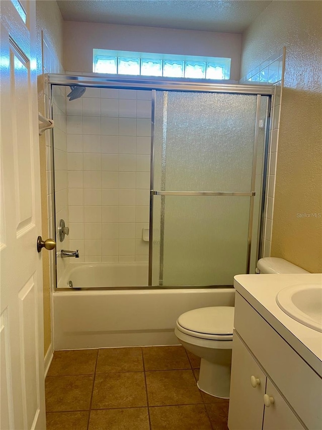 full bathroom with vanity, combined bath / shower with glass door, a textured ceiling, tile patterned flooring, and toilet