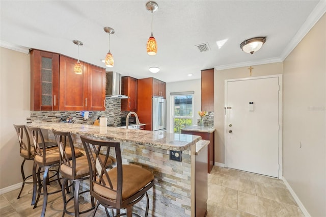 kitchen with wall chimney exhaust hood, a breakfast bar area, light stone counters, high quality fridge, and kitchen peninsula